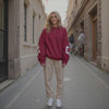 Woman wearing a red sweatshirt and beige pants standing on a city street.