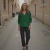 Woman in a green shirt and black pants walking down a narrow street.