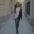 Woman walking down a city street wearing a pink sweater and black cardigan.