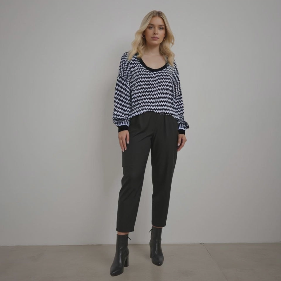 Woman wearing a black and white patterned sweater with black pants against a plain background