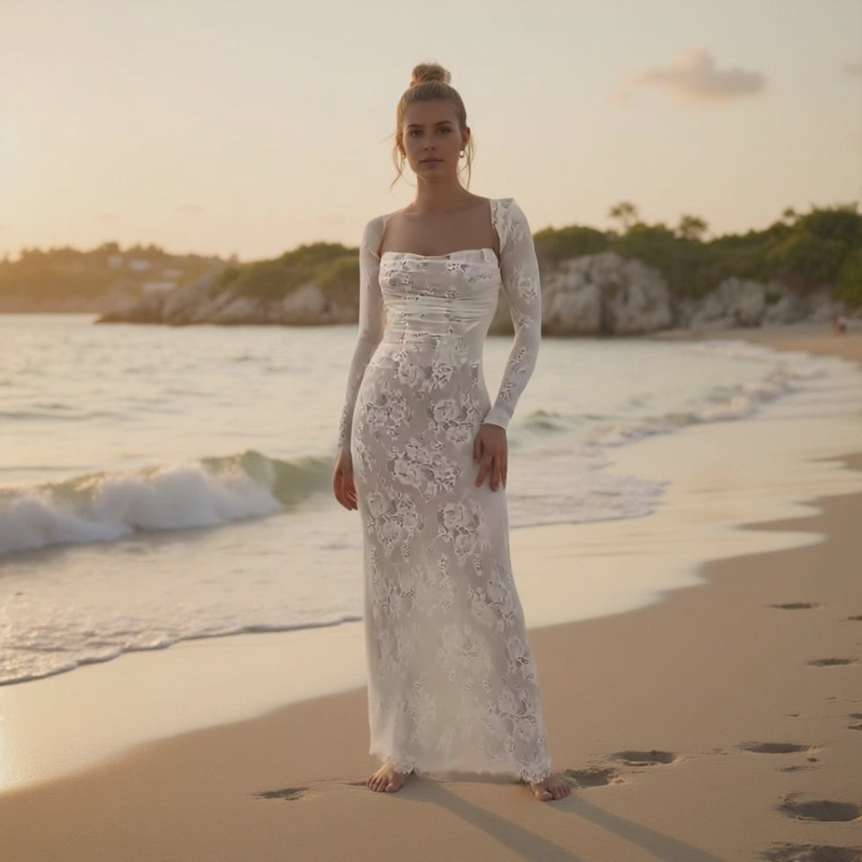 Woman in a white lace dress standing on a beach at sunset