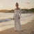 Woman in a white lace dress standing on a beach at sunset
