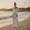 Woman in a white lace dress standing on a beach at sunset