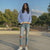 Woman wearing a blue and white striped sweater and ripped jeans standing outdoors with trees in the background.