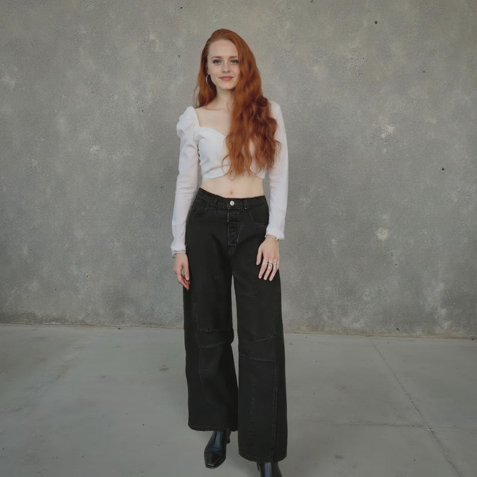Woman wearing a white top and black pants against a gray concrete wall.