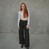 Woman wearing a white top and black pants against a gray concrete wall.
