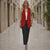 Woman in a red blazer and black pants walking down a sunlit street.