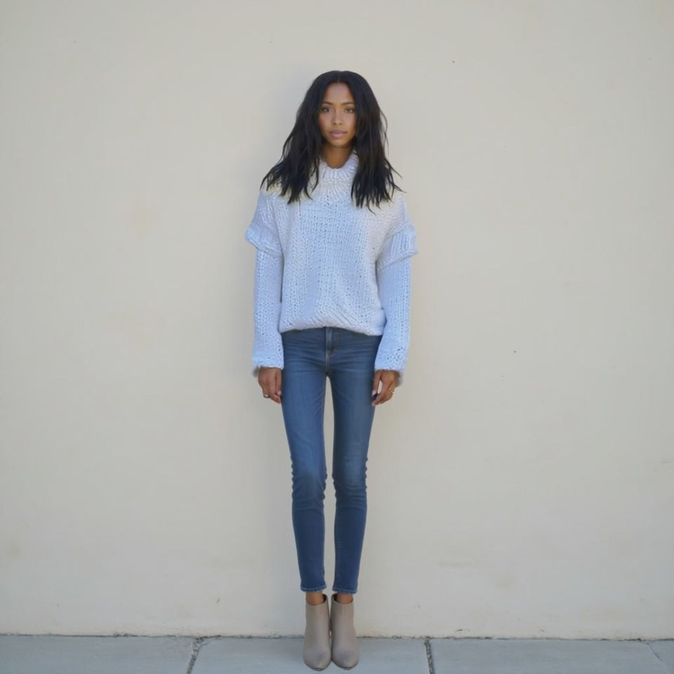Person wearing a light blue sweater and dark blue jeans against a plain background