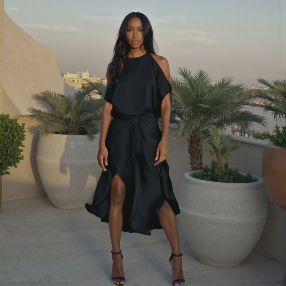 Woman in a black dress standing on a rooftop with palm trees and cityscape in the background