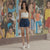 Woman in white top and blue shorts standing in front of a colorful mural.