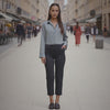 Woman standing on a city street wearing a light blue shirt and black pants.