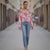 Woman walking down a street wearing a pink floral blouse and blue jeans.