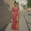 Woman in a red patterned dress standing on a street with a stone wall and building in the background.