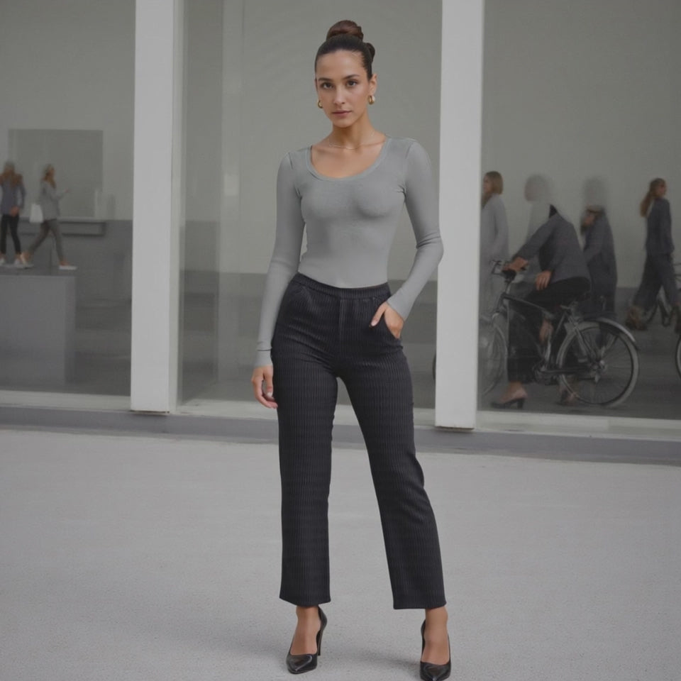 Woman in gray long-sleeve top and black pants standing in a modern indoor setting.