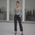 Woman in gray long-sleeve top and black pants standing in a modern indoor setting.