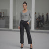 Woman in gray long-sleeve top and black pants standing in a modern indoor setting.