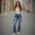 Woman with red hair wearing a white top and blue jeans standing in a narrow alley.