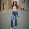 Woman with red hair wearing a white top and blue jeans standing in a narrow alley.