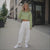 Woman in a green crop top and white pants standing on a city street.