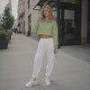 Woman in a green crop top and white pants standing on a city street.