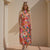 Woman wearing a colorful floral dress standing against a beige wall.