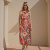 Woman wearing a colorful floral dress standing against a beige wall.