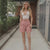 Woman in a white top and pink shorts standing on a sidewalk.