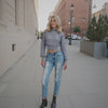 Woman in a textured sweater and ripped jeans standing on a city street.