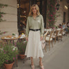 Woman standing in an outdoor cafe setting with tables and plants.