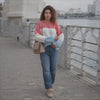Woman in a colorful sweater and jeans standing on a bridge with water and buildings in the background