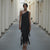 Woman wearing a black one-shoulder dress standing in a narrow alleyway.