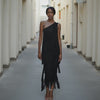 Woman wearing a black one-shoulder dress standing in a narrow alleyway.