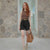 Woman with red hair standing in front of a stone wall holding a brown handbag.