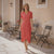 Woman in a red dress standing in an outdoor setting with chairs and a table.