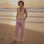 Woman standing on a beach at sunset wearing a yellow top and pink pants.