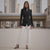 Woman wearing a black blazer and white pants standing in front of a building.