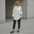 Woman wearing a white shirt and black pants standing against a neutral background