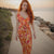 Woman in a floral dress standing on a path by a beach at sunset.