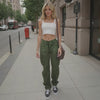 Woman in white top and green pants standing on a city sidewalk.