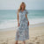Woman in a floral dress standing on a beach with ocean in the background