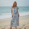 Woman in a floral dress standing on a beach with ocean in the background