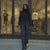 Woman in a black outfit standing in front of a clothing store with mannequins inside.