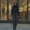 Woman in a black outfit standing in front of a clothing store with mannequins inside.