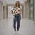 Woman wearing a cream sweater with brown heart patterns and dark blue jeans in a hallway.