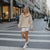Woman in a beige hoodie and white shorts walking on a city street.
