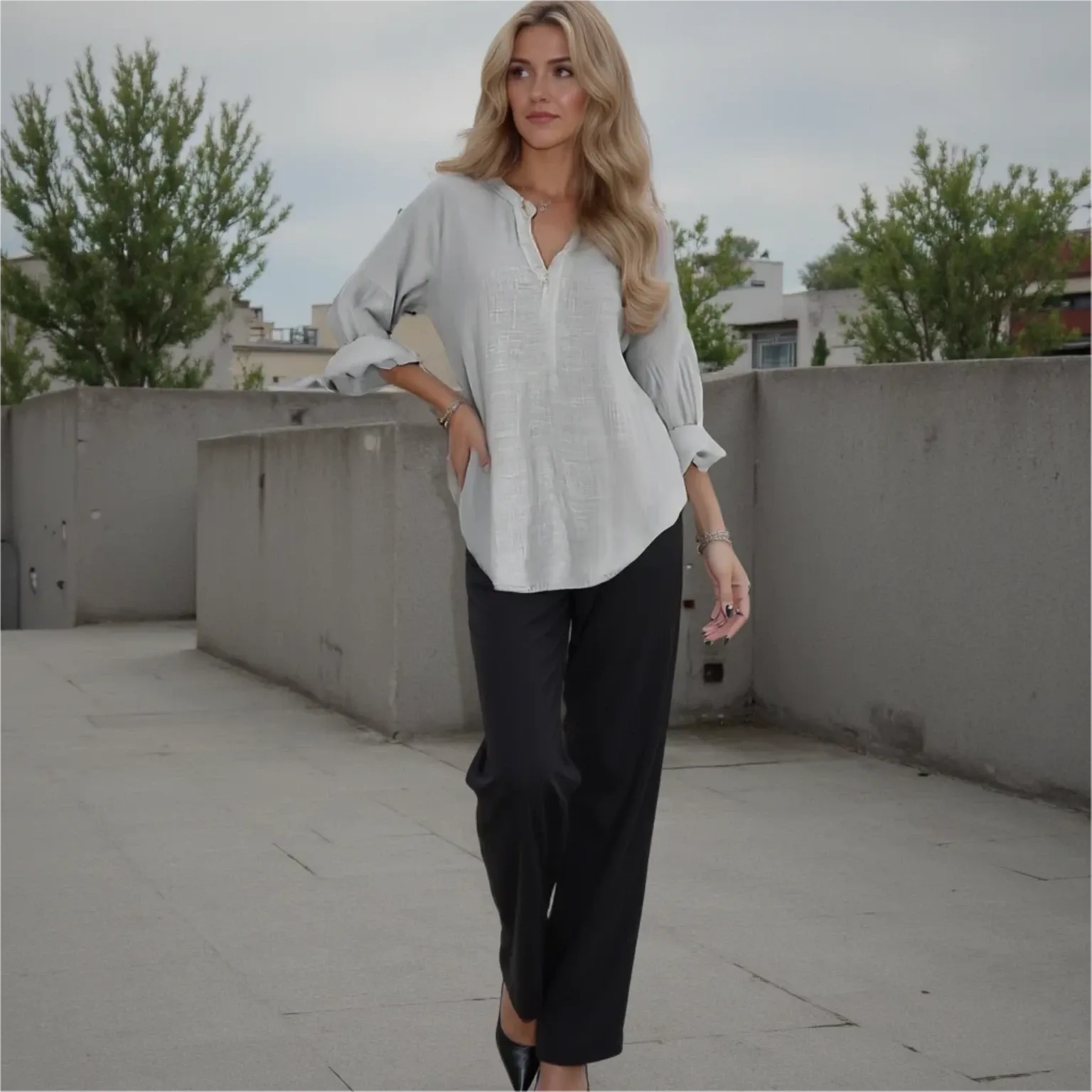 Woman in a light gray shirt and black pants standing on a rooftop with trees in the background