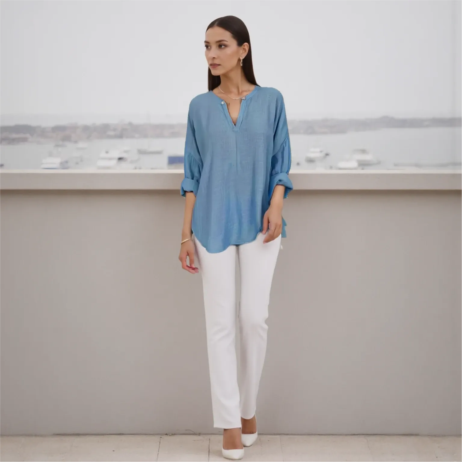 Woman wearing a blue blouse and white pants standing against a neutral background