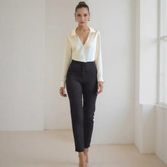 Woman wearing a white blouse and black pants in a minimalistic room.