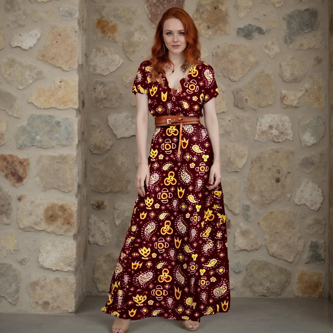 Woman wearing a patterned dress standing against a stone wall.