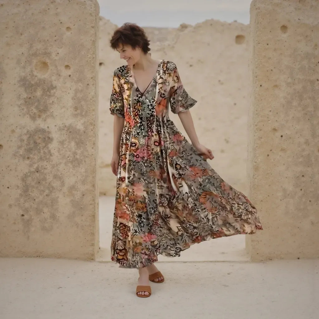 Woman in a floral dress standing in a desert-like setting with stone walls.